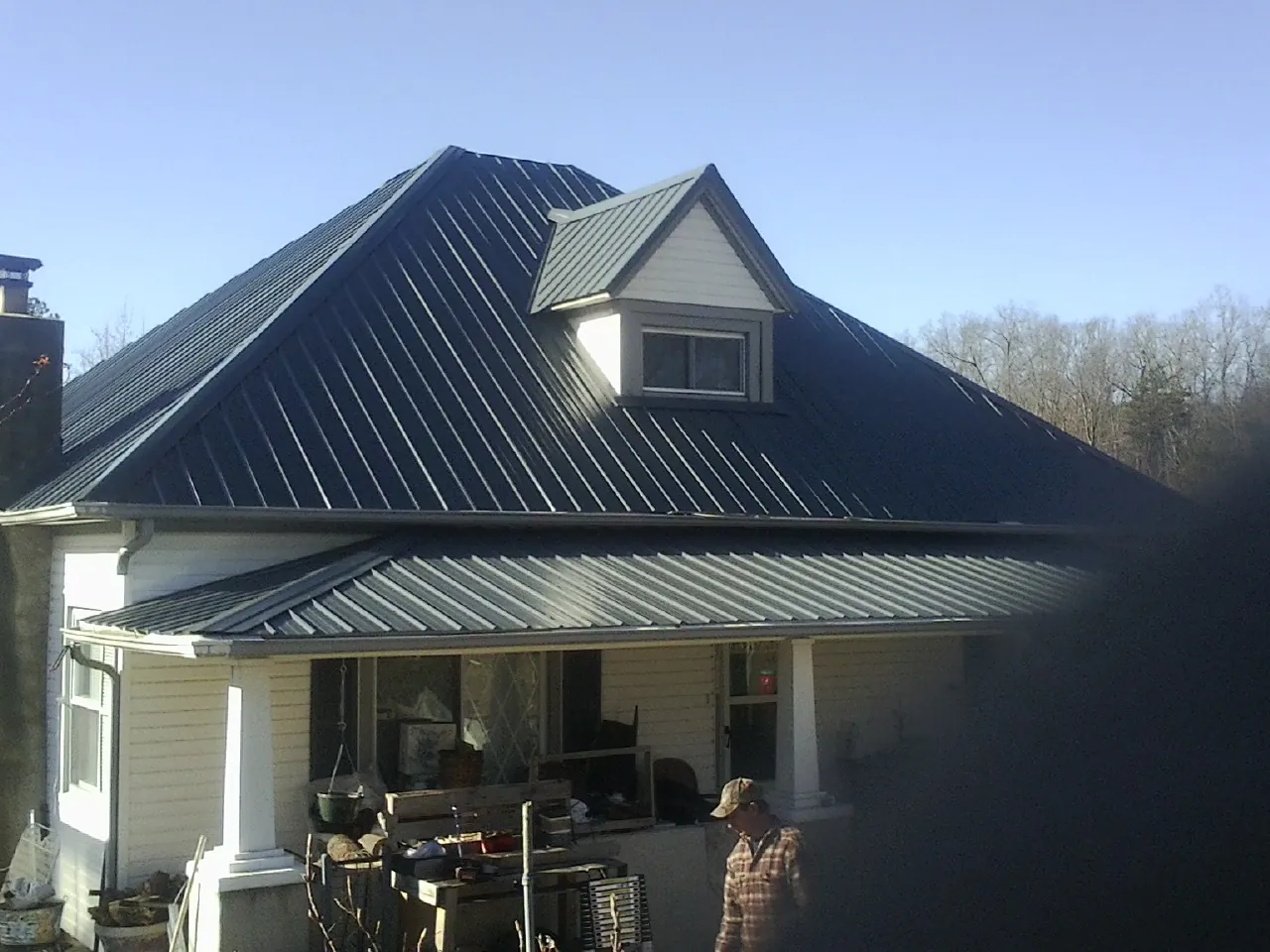 Dark blue standing seam metal roof with a dormer above a front porch in Welda