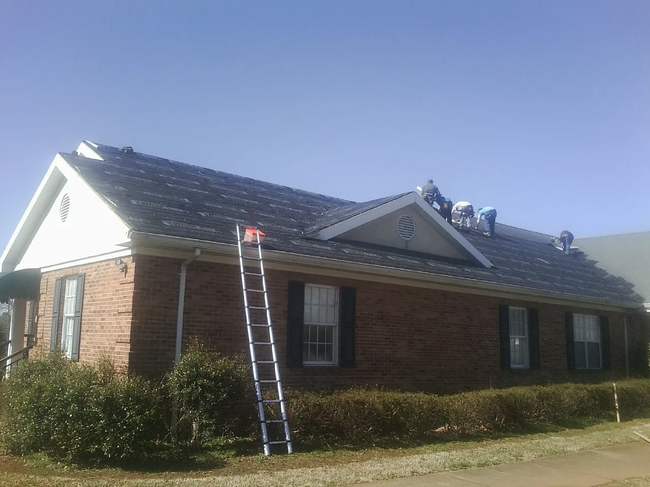 Crew tearing shingles off a brick ranch roof with a ladder set — Emergency Roof Repair work by our crew in Welda