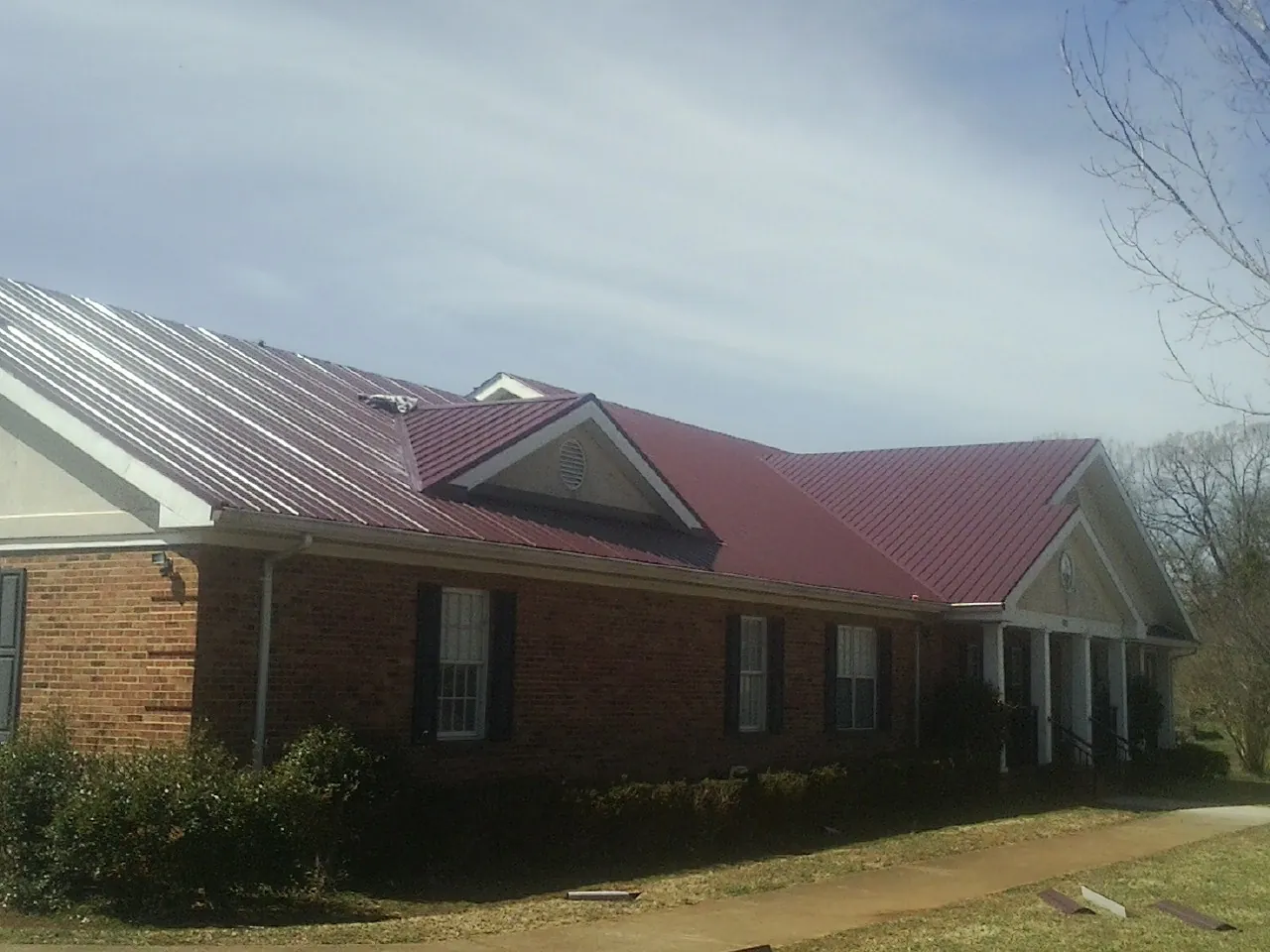 Red metal roof with gabled entries on a long brick building, from a Hail Damage Roof Repair job in Welda