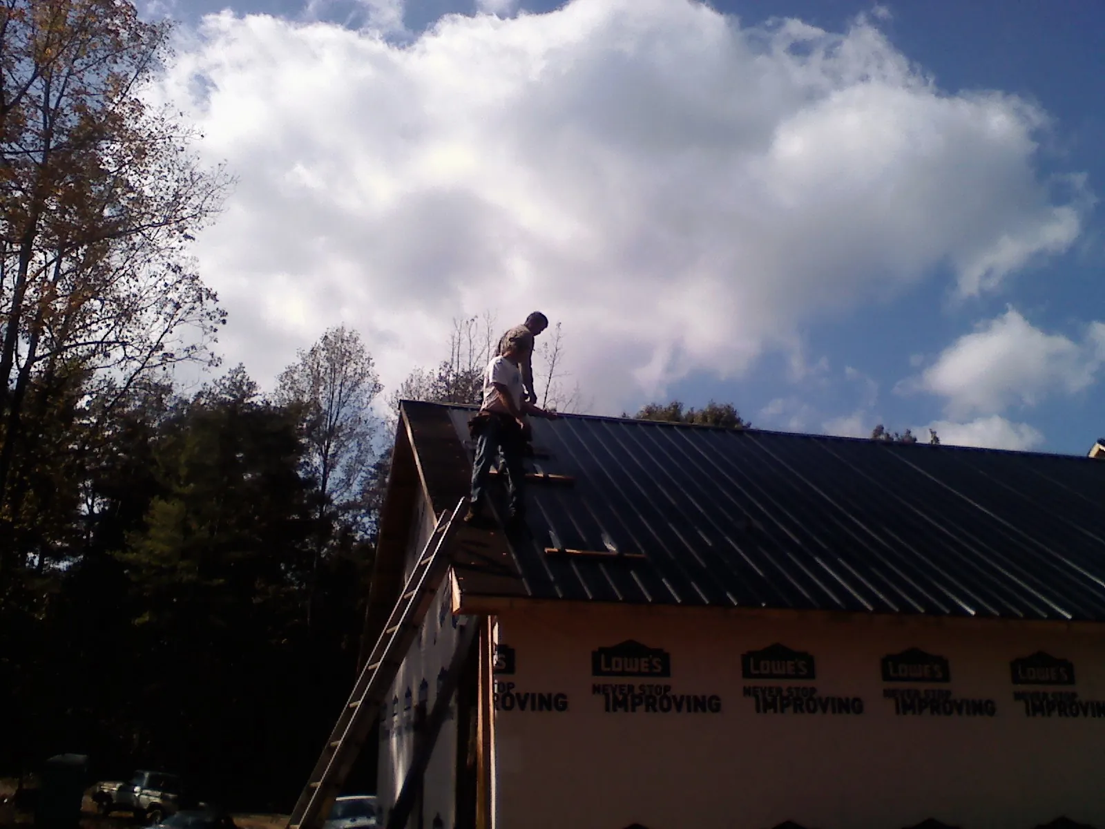 Roofer fastening dark metal panels high against a cloudy sky, from a Roof Inspection job in Welda