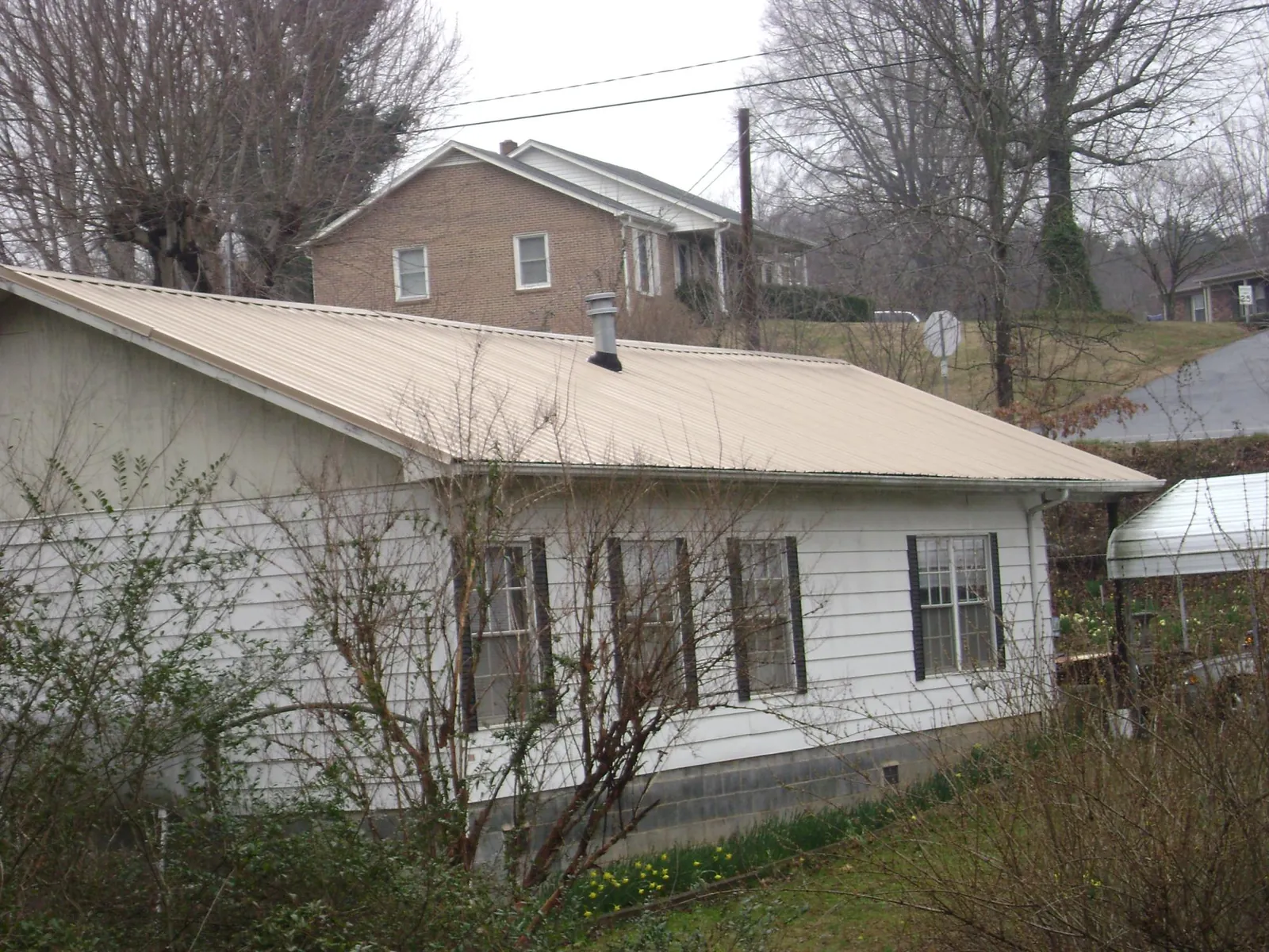 Tan metal roof on a white sided house set into a hillside — Commercial Roofing by Roofing Brothers in Welda